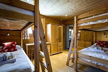 A cozy wooden cabin bedroom with two rustic bunk beds, white linens, red pillows, and matching pine furniture.