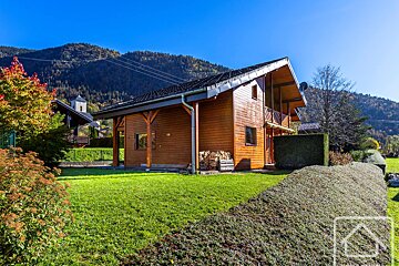 A wooden house with mountains in the background is for sale