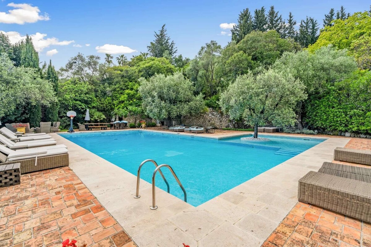 Scenic Mediterranean outdoor pool with bright blue water, surrounded by abundant green trees, lounge chairs, and a distinctive tree growing in the pool itself.