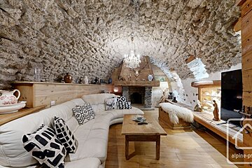 A rustic living room with a natural stone vaulted ceiling, white curved sofa, wooden fireplace, and an elegant chandelier. A cozy, cave-like retreat.