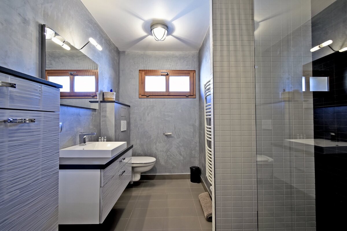 Modern gray bathroom featuring a floating sink vanity, wall-mounted toilet, small window, and tiled glass shower.