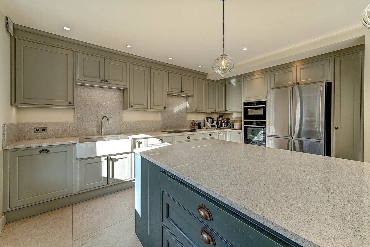 Spacious, modern kitchen with sage green cabinets, light countertops, a blue island, and stainless steel appliances.