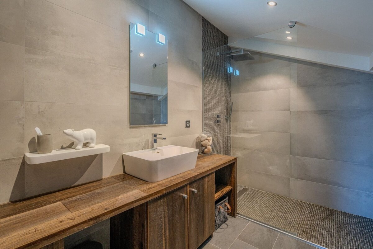 Contemporary bathroom with light grey tiles, a wooden vanity holding a white vessel sink, and a spacious walk-in glass shower.