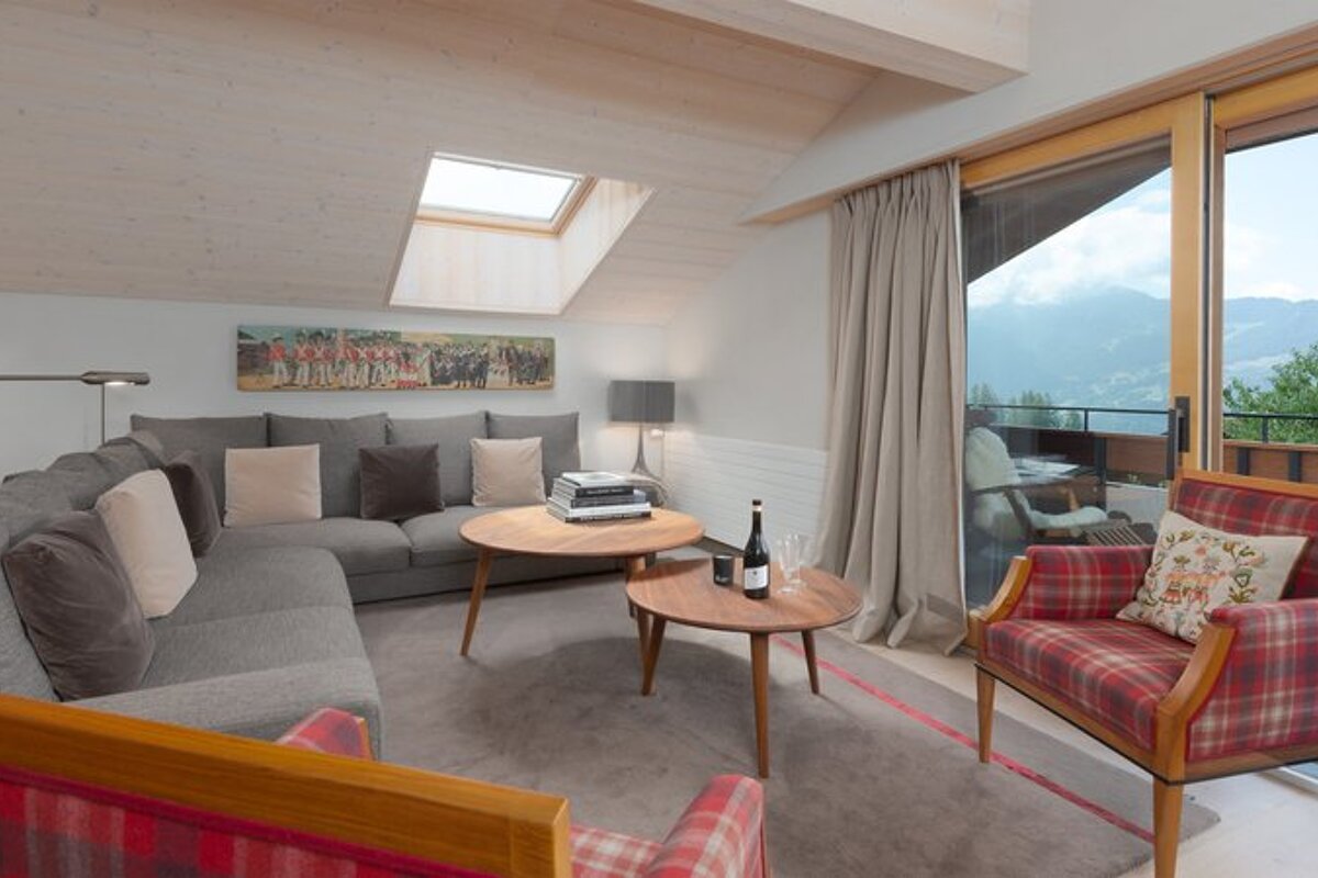 Cozy attic living room with a grey sectional, red plaid armchairs, round coffee tables, a skylight, and beautiful mountain views.