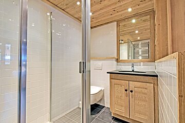 Chalet-style bathroom featuring a glass shower, white tiled walls, a wooden vanity, and a rustic wood-paneled ceiling.