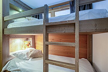 Rustic wooden bunk beds with white sheets, a built-in ladder, and a teddy bear sitting on the lower bunk.