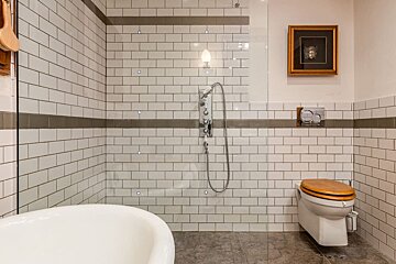 A bathroom with white tiles and a picture on the wall above the toilet