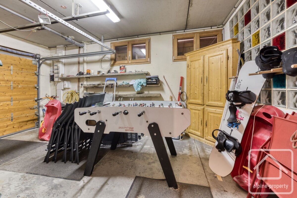 A garage/storage room featuring a foosball table, snowboard, helmets, sleds, shelves, and wooden cabinets, with a rolling garage door.