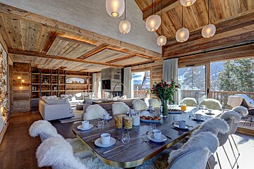Cozy, open-plan ski chalet with rustic wood interiors, a breakfast table, inviting living space, and panoramic snowy mountain scenery.
