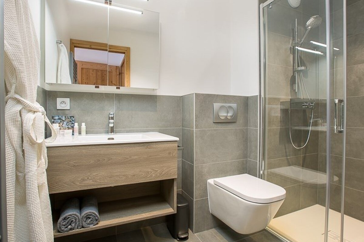 A modern bathroom featuring a wooden vanity, a wall-mounted toilet, and a glass walk-in shower.