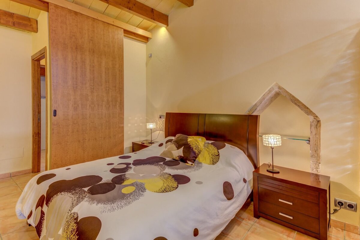 A bedroom with a bed and a nightstand with a lamp on it