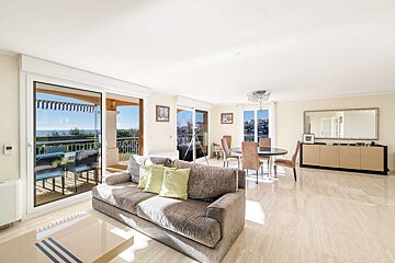 Bright, modern living-dining room with a grey sofa, dining table, and large sliding doors to a balcony with a stunning sea view.