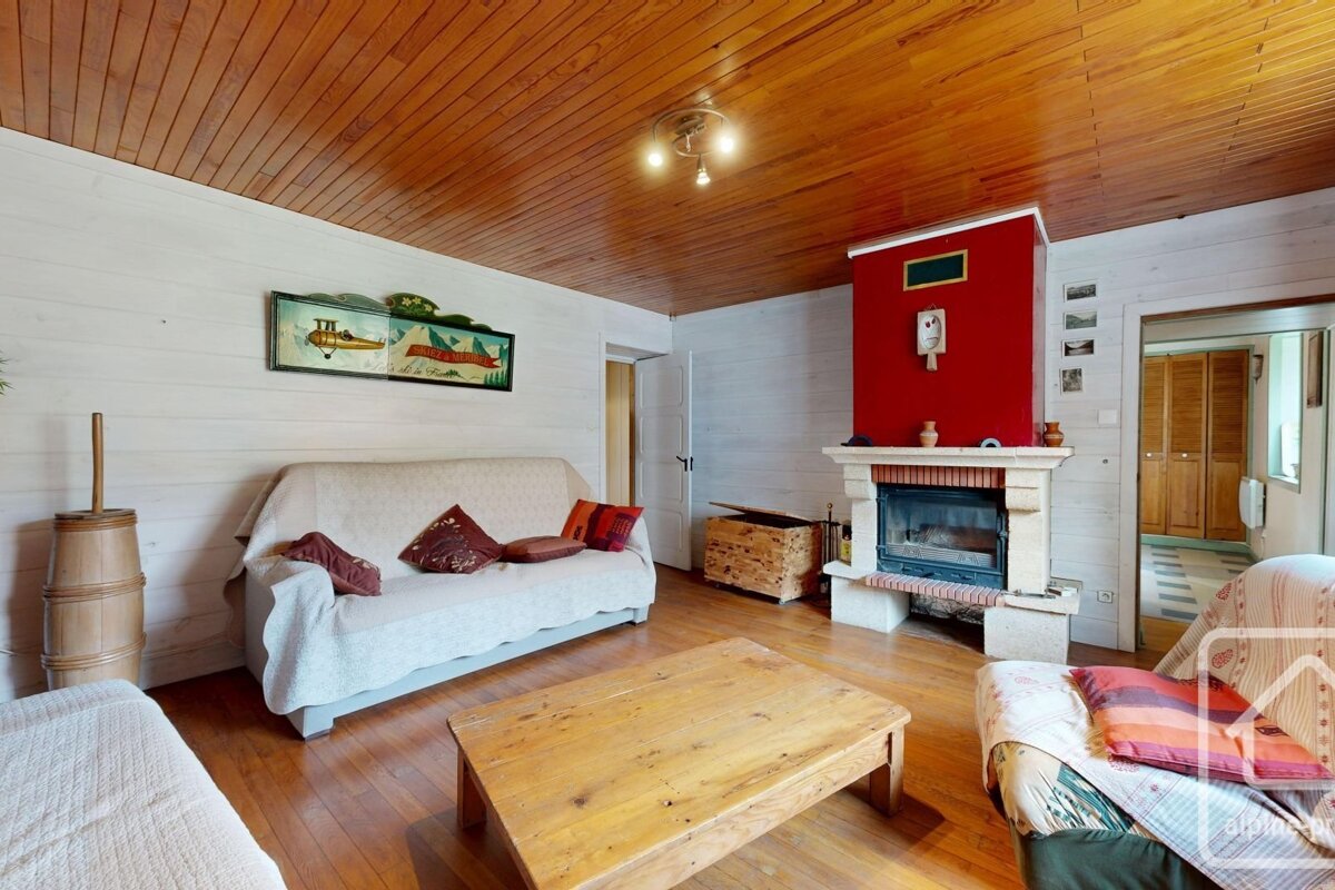 Cozy, rustic living room featuring a wood-paneled ceiling, white plank walls, a striking red fireplace, sofa, and wooden coffee table.