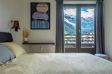 A bedroom with a bed and a window with mountains in the background