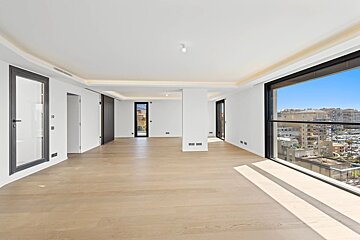 Spacious, empty modern apartment featuring light wood floors, white walls, and large floor-to-ceiling windows overlooking a city view.