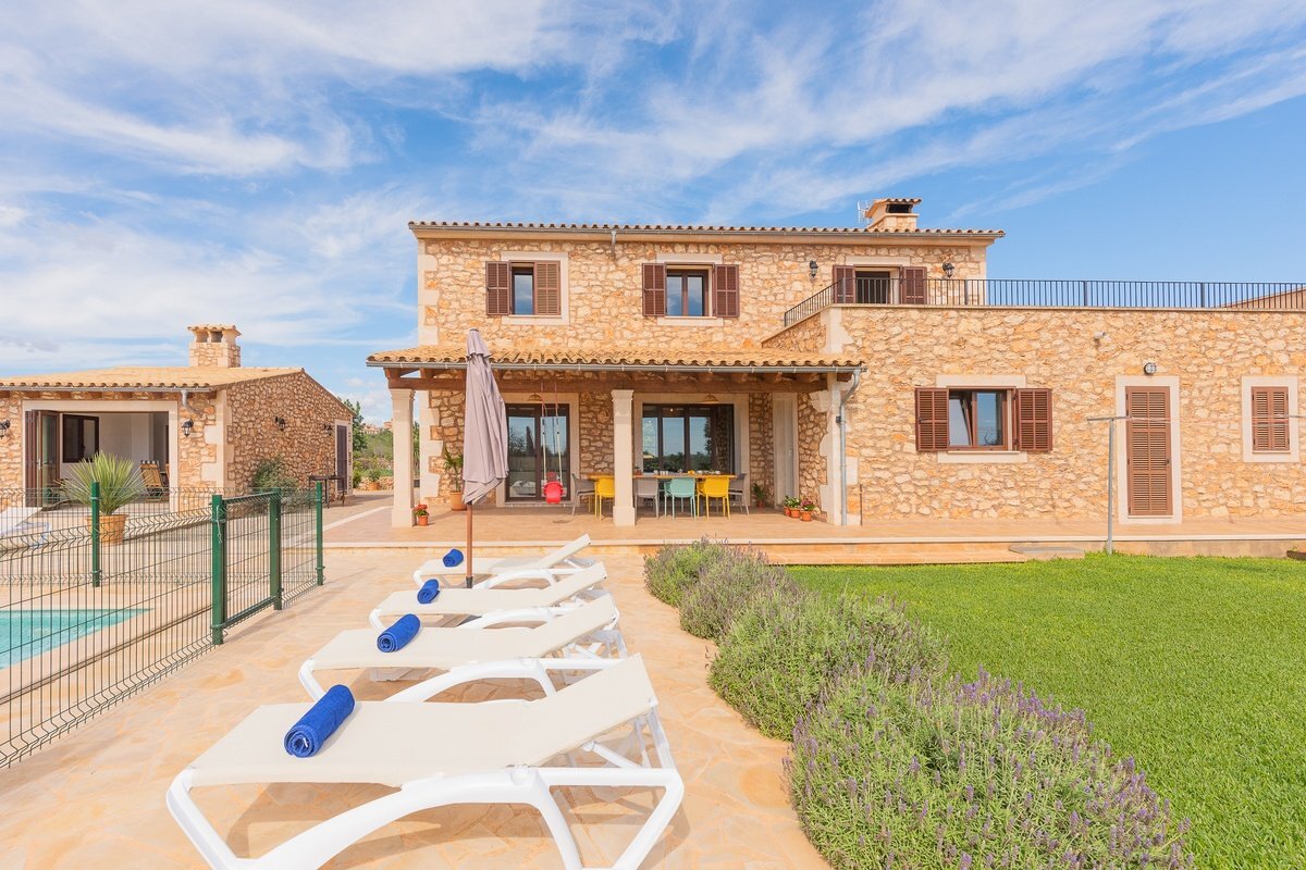 A row of white lounge chairs are lined up in front of a large stone house