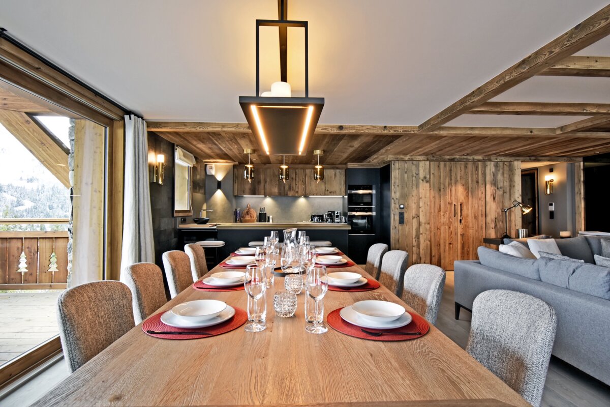 A cozy, modern alpine chalet dining room with a long wooden table, elegant lighting, and warm wood-paneled walls.