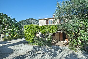 A stone house is surrounded by trees and bushes