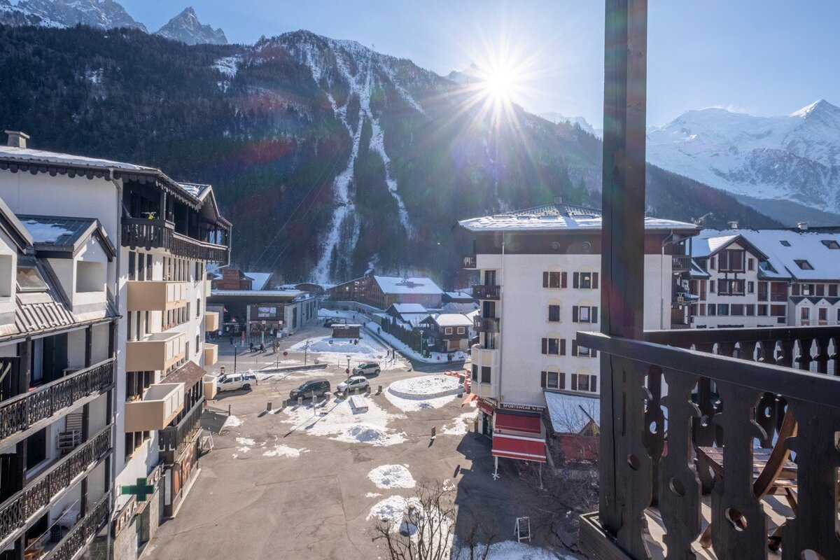 Sunny alpine town with majestic snow-capped mountains, visible from a balcony, with bright sun shining overhead.