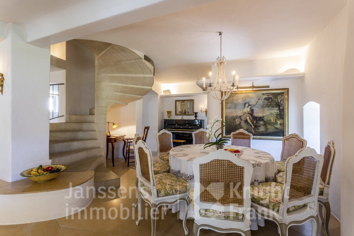 A dining room with a spiral staircase and janssens immobilier written on the wall