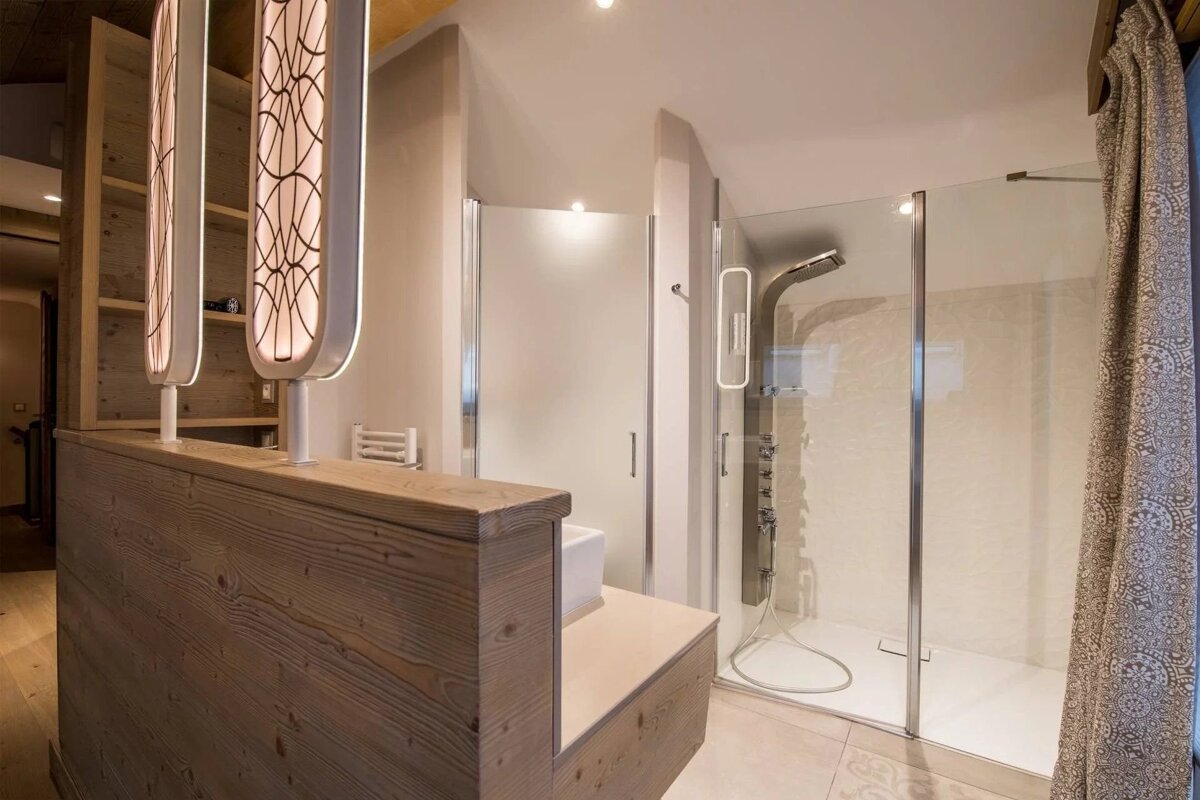 A stylish bathroom with a wooden partition, two illuminated ornate panels, and two glass shower enclosures, one with a modern shower column.