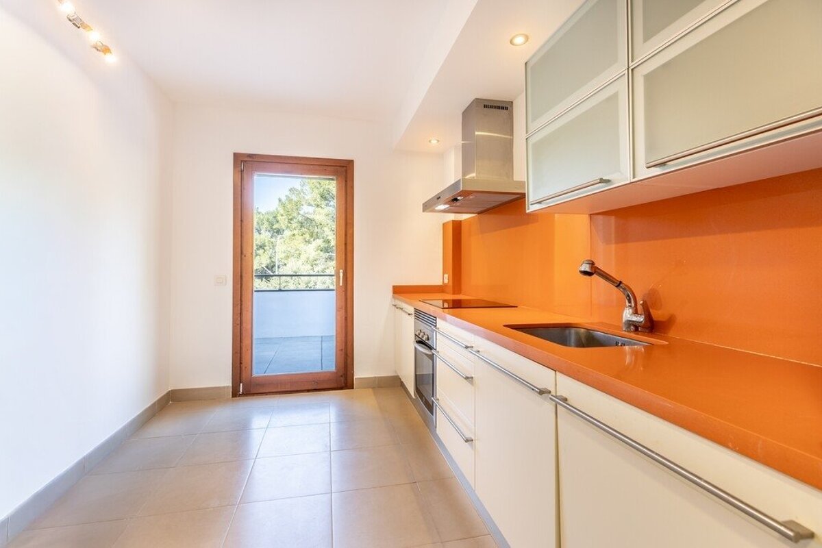 A modern kitchen featuring cream cabinets, a bright orange countertop and backsplash, and a glass door leading to a balcony.