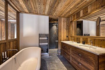 A chic, rustic chalet-style bathroom featuring warm wood walls and ceiling, a freestanding tub, double vanity, and a modern glass shower.
