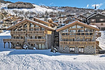 Beautiful stone and wood chalets in a snow-covered alpine village on a bright, sunny winter day.