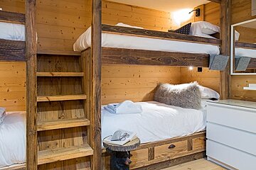 Cozy rustic bedroom featuring built-in wooden bunk beds with white bedding, a wooden ladder, and warm pine paneled walls.