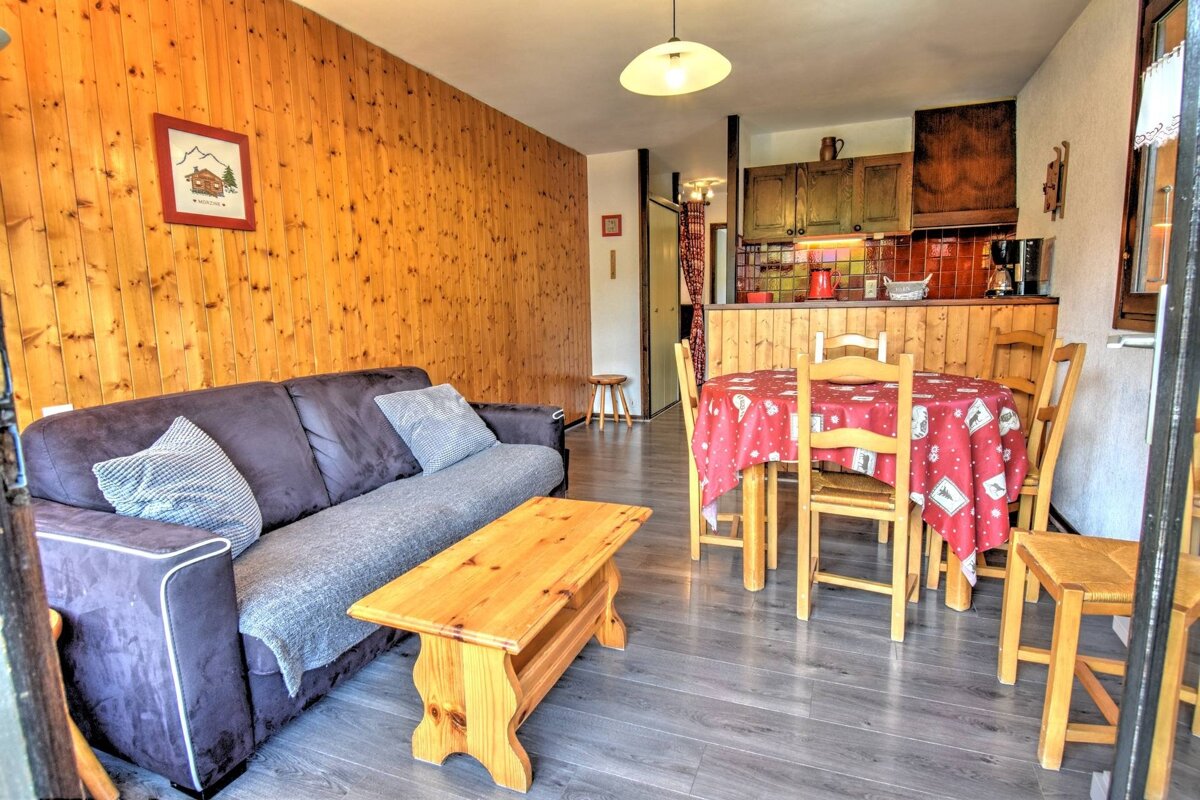 Rustic apartment interior with wood-paneled walls, a gray sofa, and a dining table with a red tablecloth.