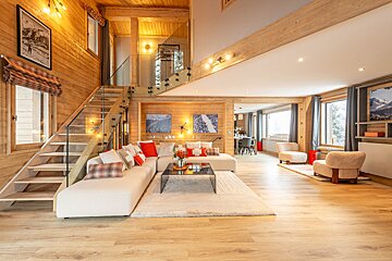 Cozy, modern wooden chalet living room featuring a white sectional, glass-railed staircase, and warm, bright lighting.