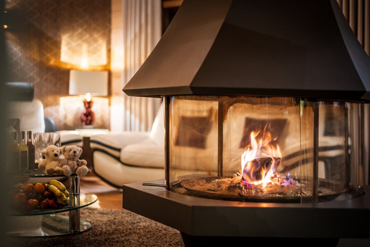 A roaring fire in a modern glass fireplace warms up a cozy, luxury living room with plush white sofas.