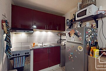 A compact kitchen featuring dark red cabinets, white subway tile backsplash, a stainless steel sink, stove, and a refrigerator.