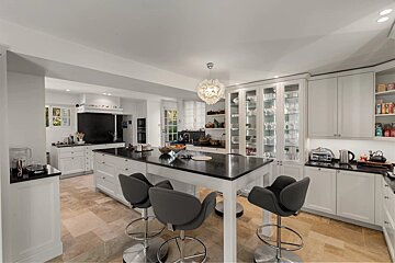 Spacious, modern kitchen with white cabinets, dark countertops, a large island with bar stools, and stone tile flooring. Bright and inviting.
