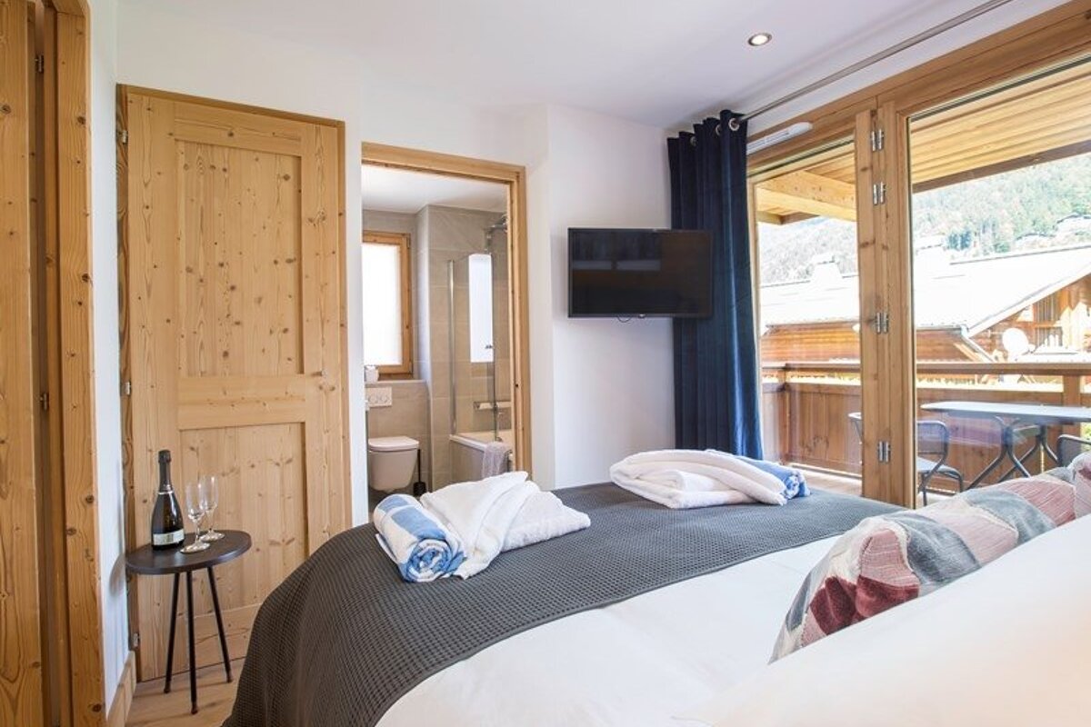 Cozy wooden bedroom with a large bed, ensuite bathroom, and balcony access in a mountain chalet.