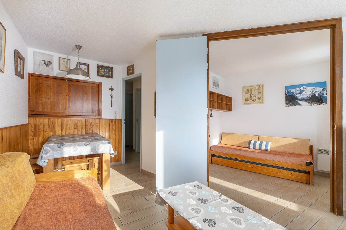 Bright, cozy living area with a rustic dining nook, wooden daybeds, and wall art, separated by a light blue partition.
