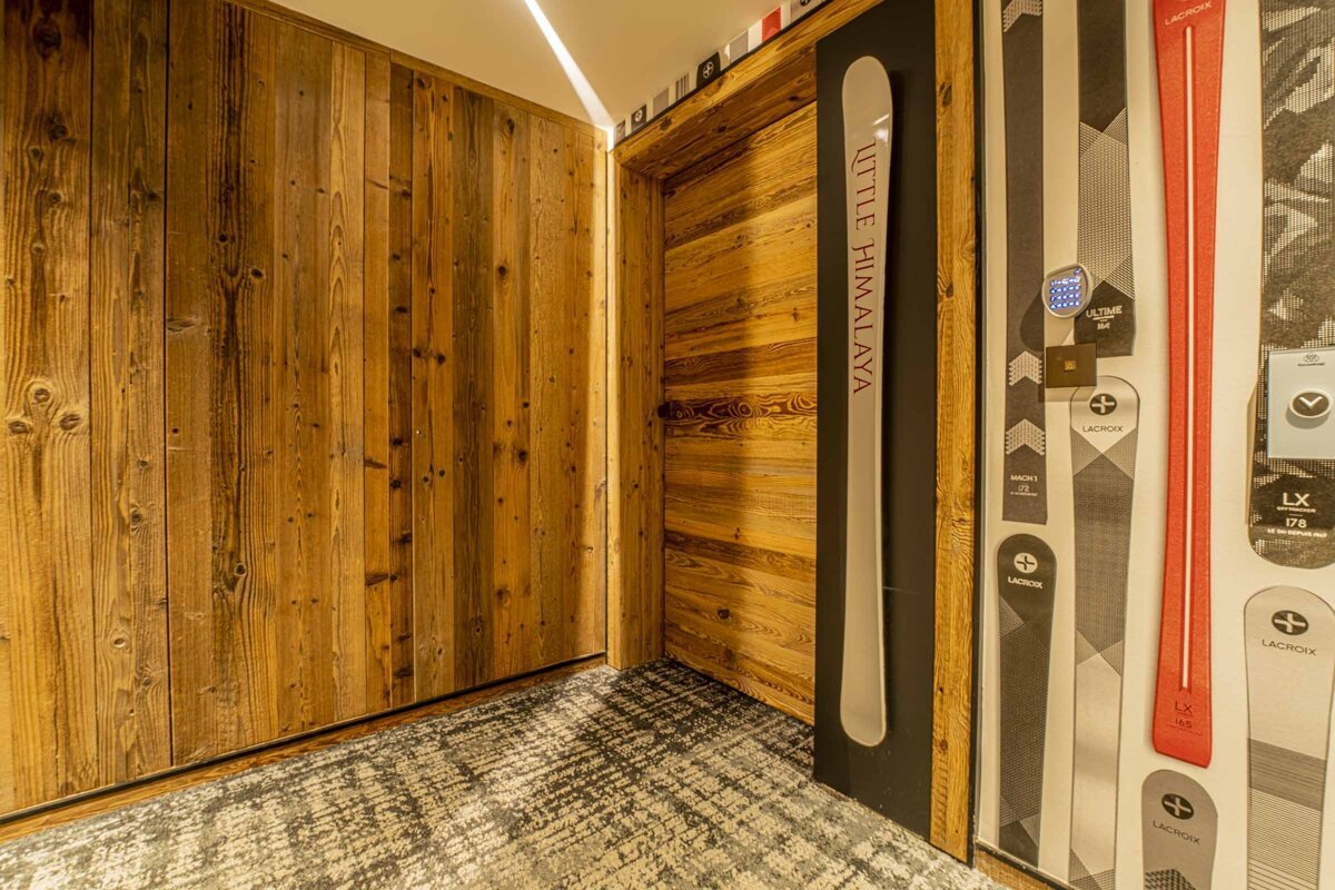Rustic ski lodge interior featuring wood-paneled walls, a decorative 'Little Himalaya' ski, and ski-themed wallpaper.