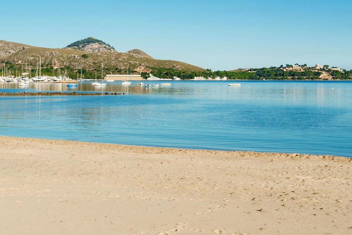 A beach with boats in the water and mountains in the background