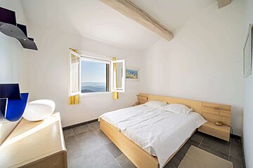 Bright, modern bedroom with a light wood bed, white walls, and a large window offering a stunning mountain view. Gray tiled floor and unique decor.