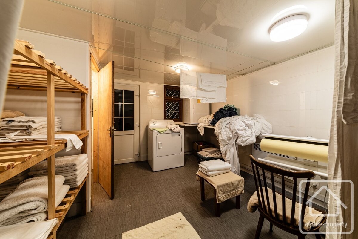 A well-used laundry room with a washing machine, dryer, wooden shelves with stacked towels, piles of laundry, and clothes hanging to dry.