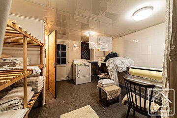 A well-used laundry room with a washing machine, dryer, wooden shelves with stacked towels, piles of laundry, and clothes hanging to dry.