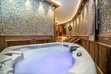 Luxurious spa room with a glowing hot tub, wooden paneling, and mosaic tiled walls. Warm accent lighting creates a cozy ambiance.