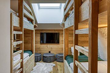 Cozy room with facing wooden bunk beds, a TV on wood-paneled walls, a skylight, grey poufs, and a white fluffy rug.