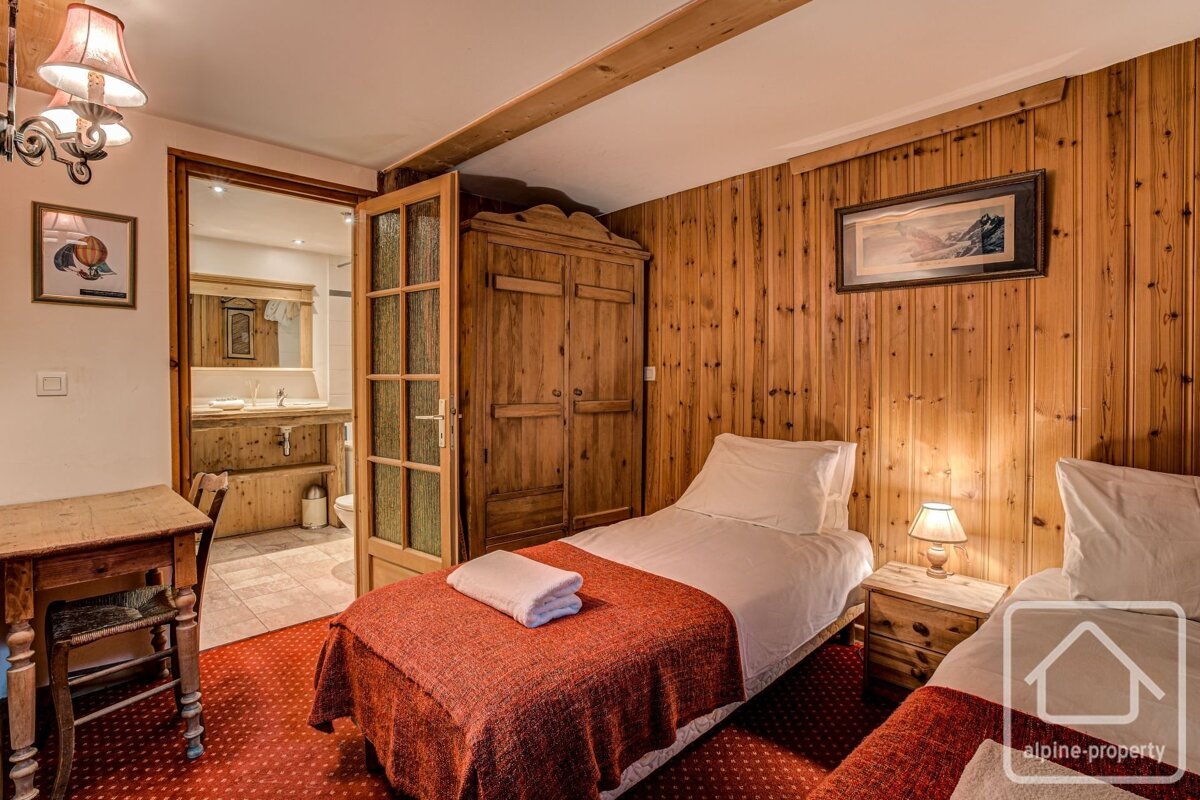 A rustic twin bedroom with wood-paneled walls, red carpet, and an en-suite bathroom visible through an open door.