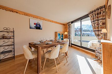 Cozy alpine dining room featuring a wooden table, fluffy white chairs, and large windows with scenic mountain views.