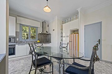 A bright kitchen-dining area featuring a glass table with ornate chairs, a modern kitchen with a window view, and a colorful retro-striped fridge.
