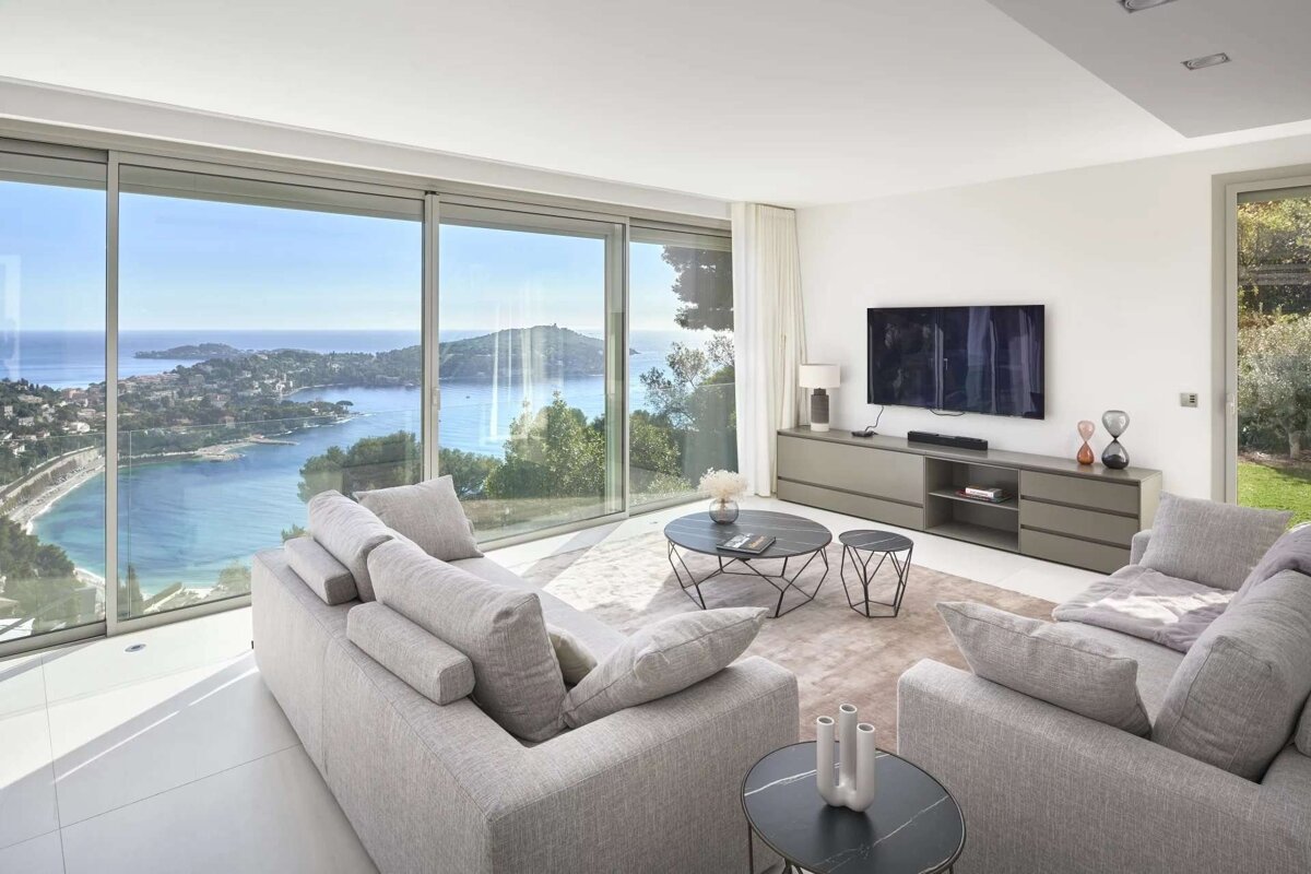 Modern living room with expansive windows offering a stunning panoramic view of a coastal bay and landscape.