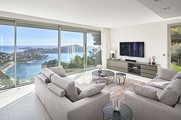 Modern living room with expansive windows offering a stunning panoramic view of a coastal bay and landscape.