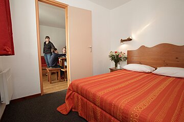 A bedroom with a red bed and a wooden headboard