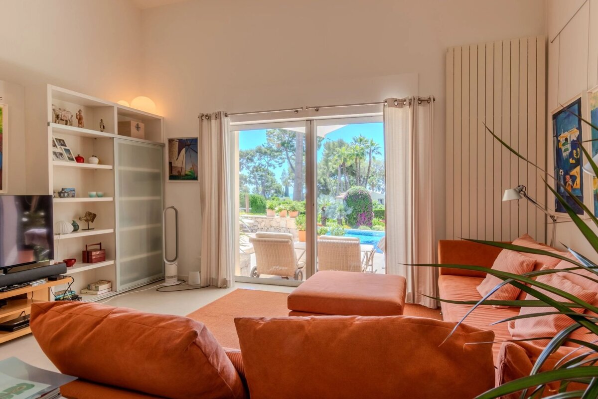 A living room with orange sofas, opening onto a sunny terrace with a pool.
